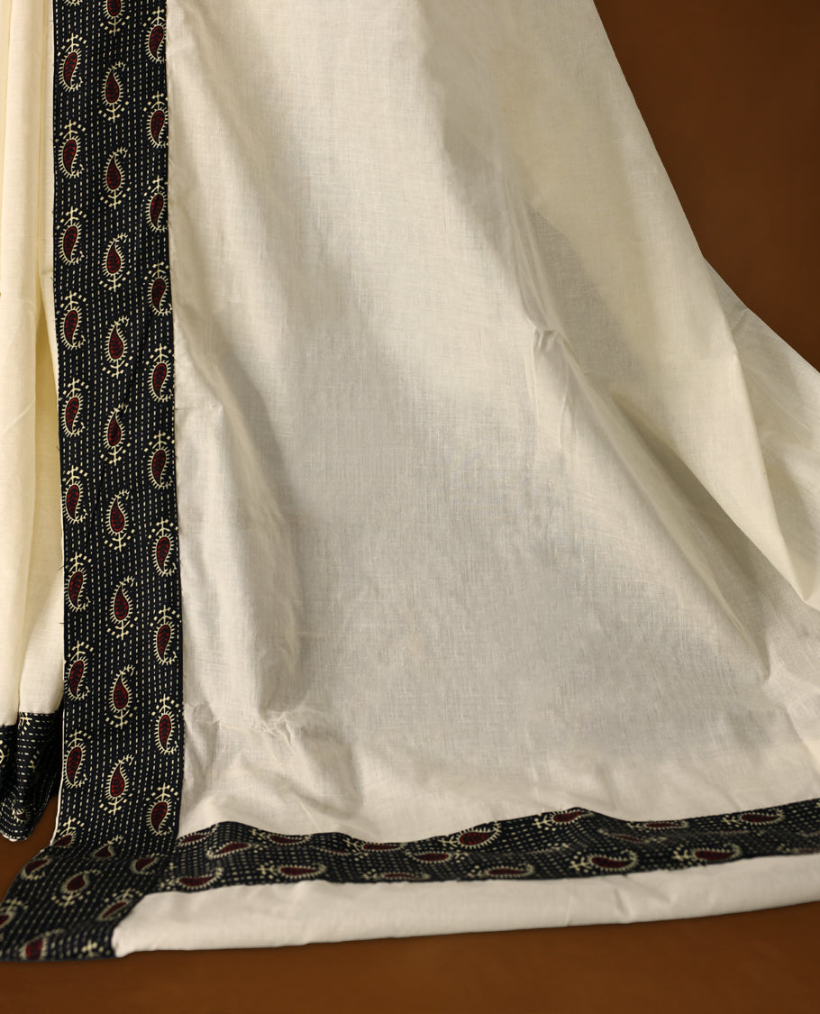 Off white colour cotton Kerala saree accentuated with a black printed border featuring red paisley motifs and delicate white dotted patterns, paired with a matching printed blouse for a classic ethnic charm