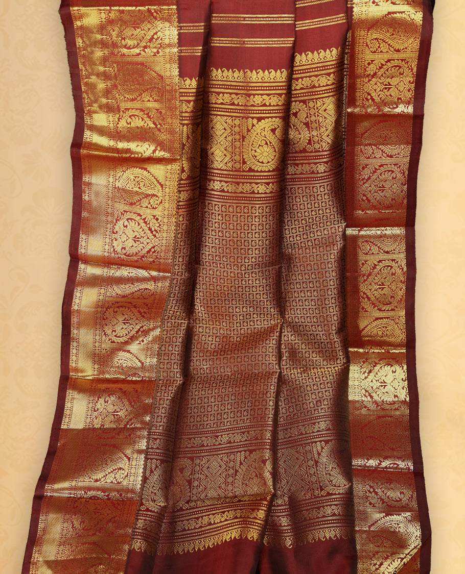 Deep maroon colour pure Kancheepuram traditional saree featuring gold zari Mayoora Chakra motifs across the body, enhanced with a classic traditional border with Peacock and mango design and a grand pallu with Mango designs, paired with a matching blouse.