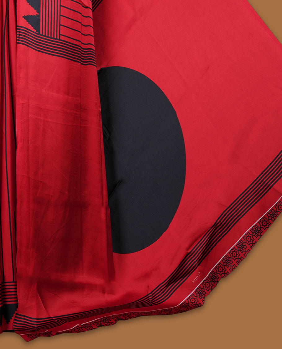 Red colour semi modal saree featuring black colour geometric borders and fine stripe detailing, finished with an oversized circular motif on the pallu, paired with a matching printed blouse.