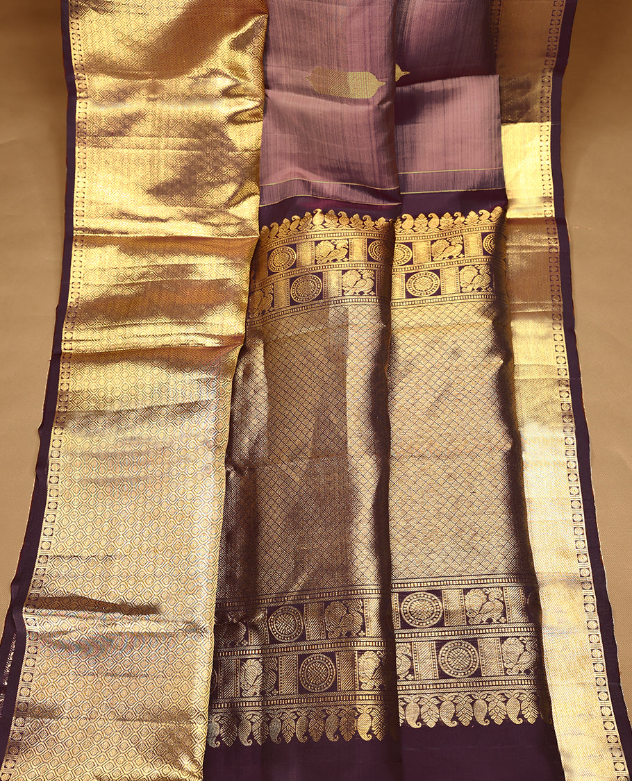 Muted mauve Colour traditional Kancheepuram silk saree adorned with antique zari traditional motifs on the body, featuring a contrasting border with Rich floral and geometric patterns, and paired with a matching blouse.