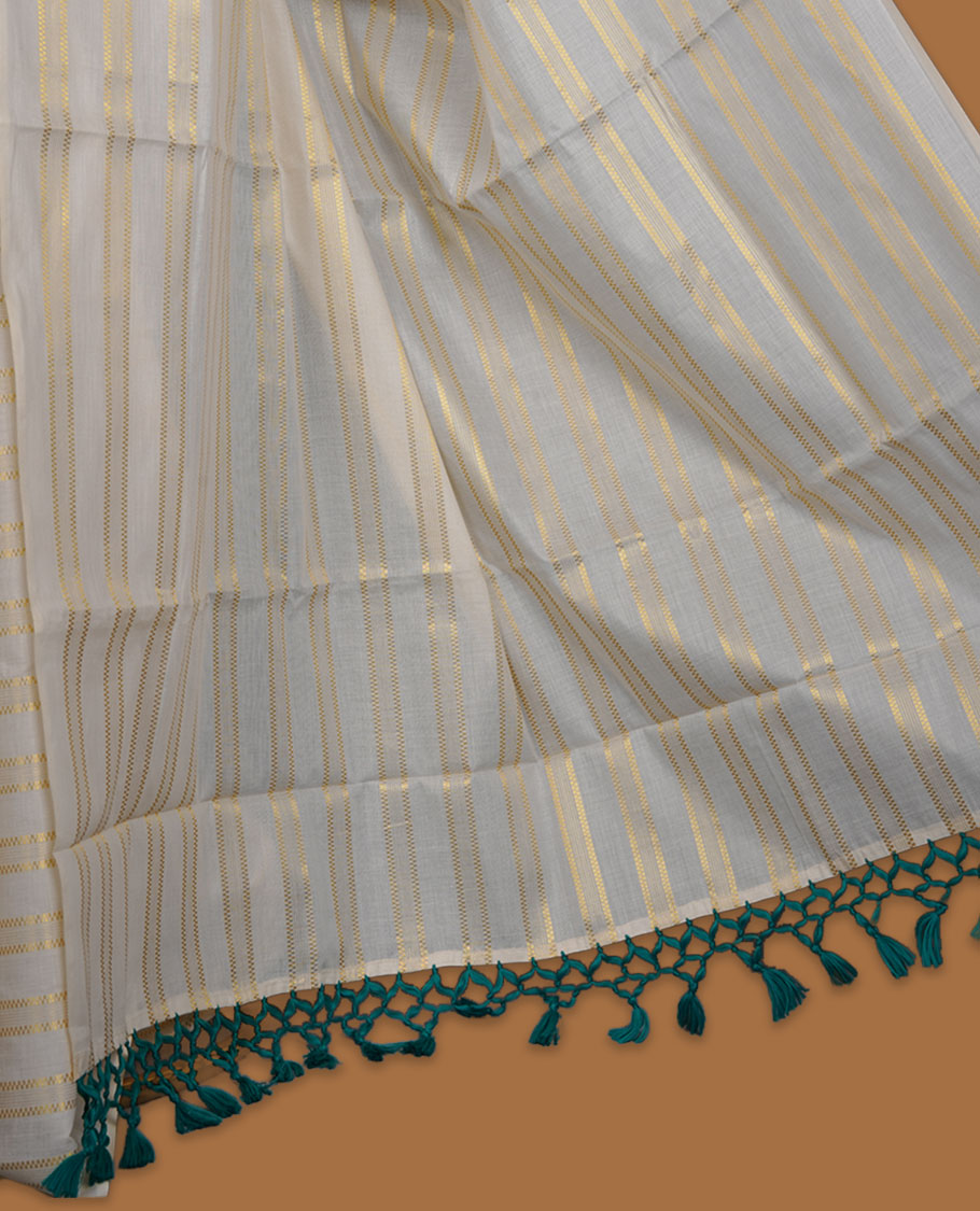 Off-white colour cotton Kerala saree featuring subtle gold zari stripe detailing across the body, finished with elegant green tassels on the pallu, and paired with a matching blouse.