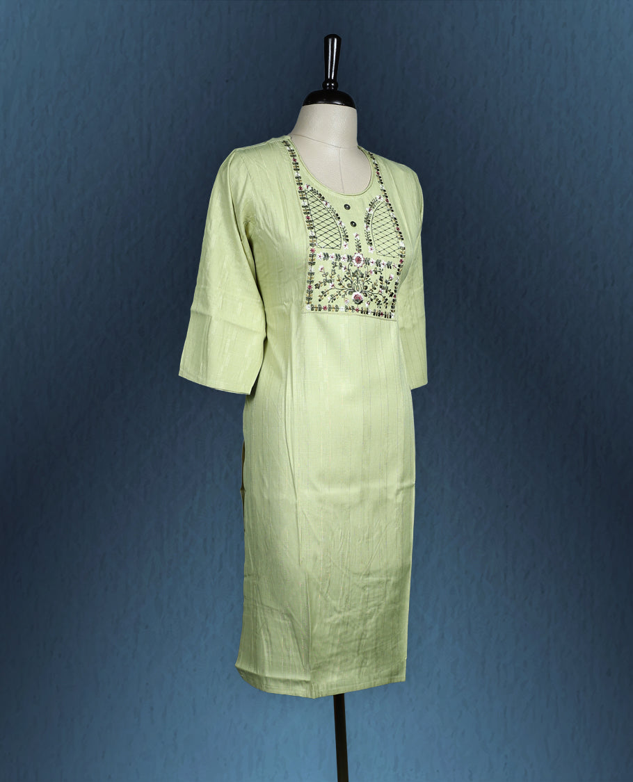 Light green colour kurti with subtle vertical self stripes, highlighted by an intricately embroidered yoke in floral and geometric patterns, featuring a round neckline with button accents and three quarter sleeves.