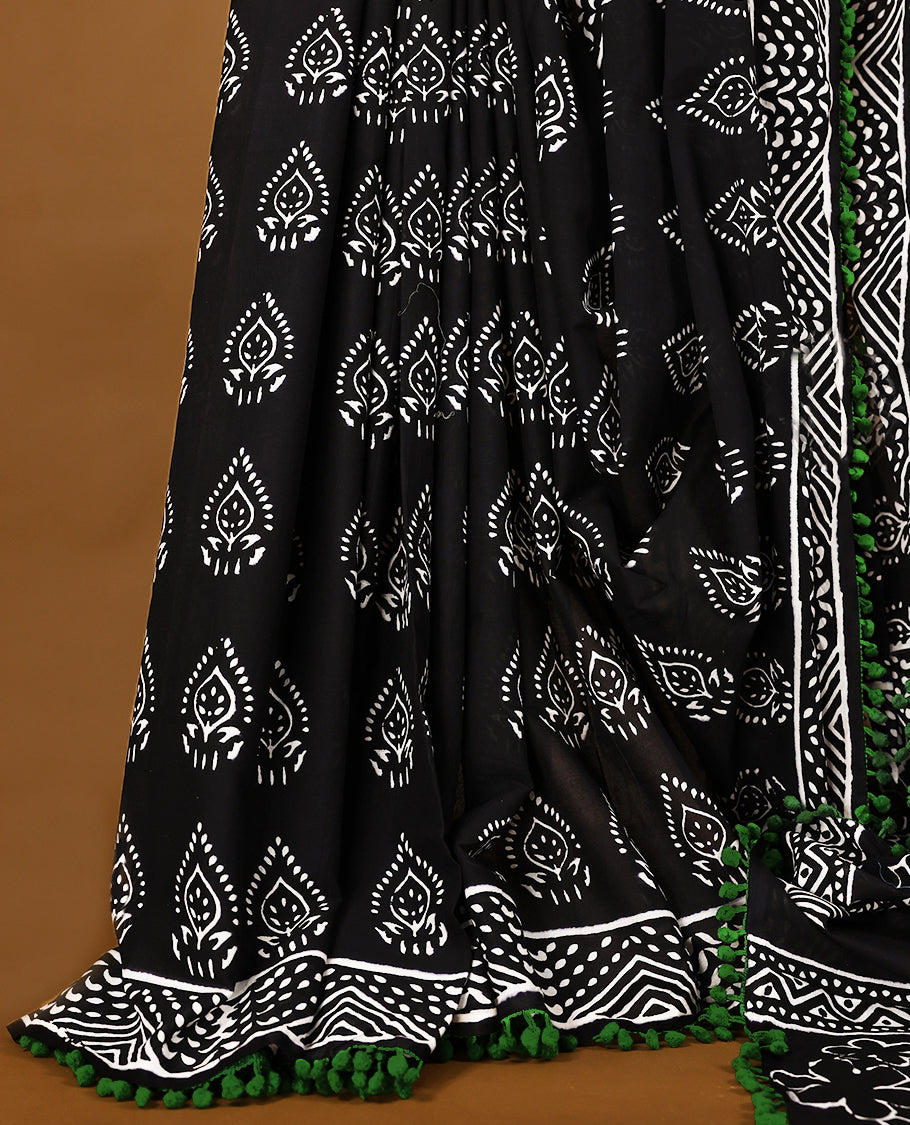 Black cotton saree features intricate white handblock prints, a beautifully detailed border with Green piping and Self Coloured Blouse