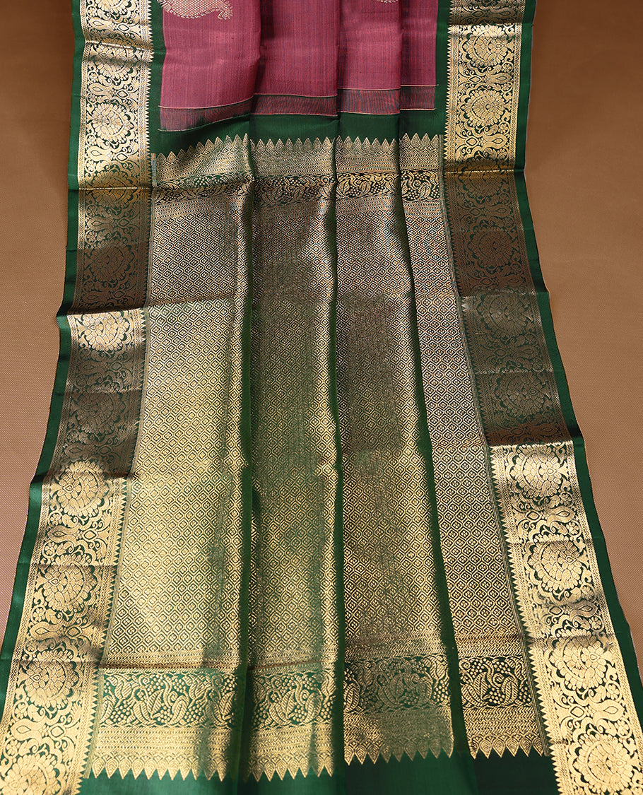 Solid mauve pink colour traditional Kancheepuram silk saree adorned with antique zari paisley motifs on the body, featuring a deep bottle green border with antique gold zari floral and vine patterns, and paired with a matching blouse.