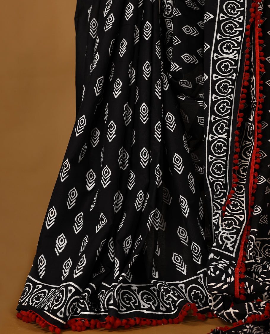Black cotton saree features intricate white handblock prints, a beautifully detailed border with red piping and Self Coloured Blouse