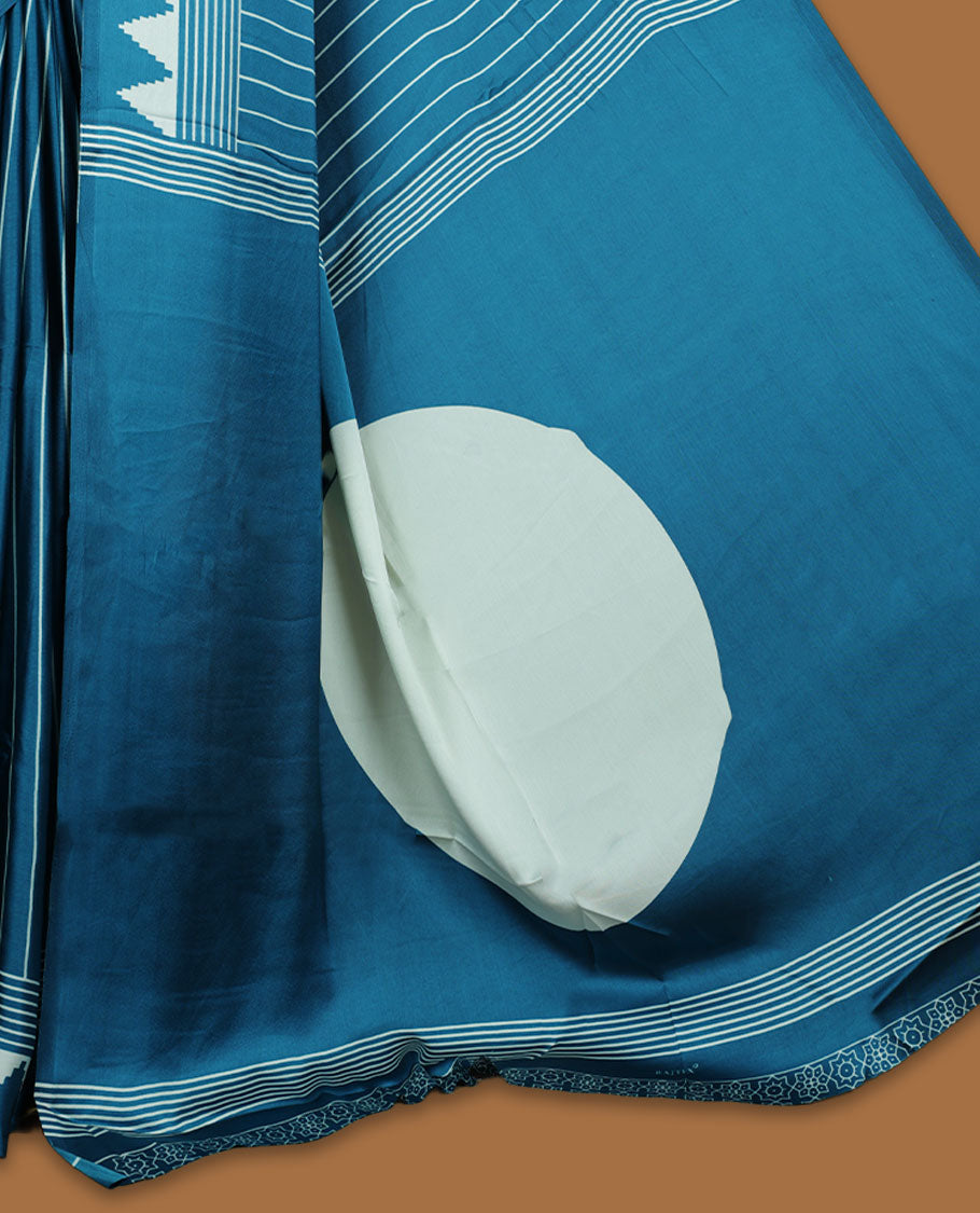 Teal Blue colour semi modal saree featuring bold white geometric borders and fine stripe detailing, finished with an oversized white circular motif on the pallu, paired with a matching printed blouse.