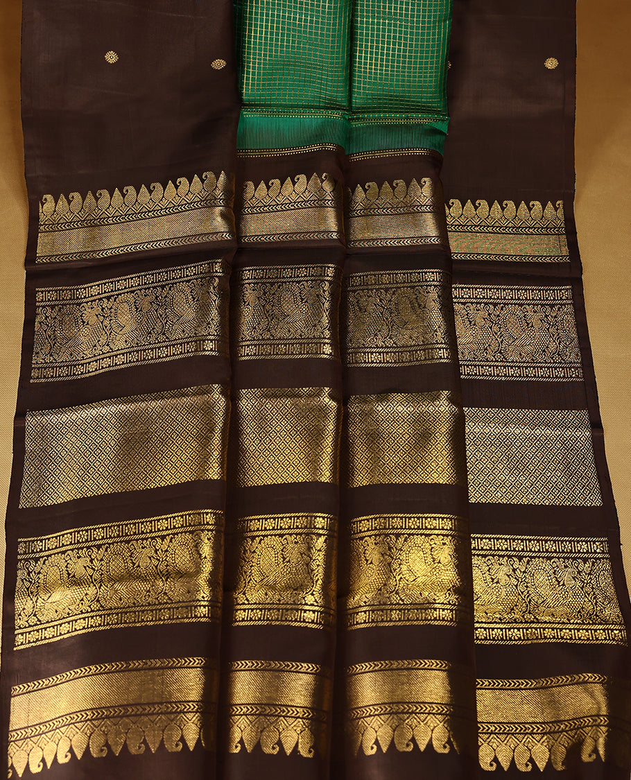 Green Colour pure traditional Kancheepuram silk saree featuring antique zari checks on the body, beautifully complemented by a dark chocolate simple border with delicate Chakkram and peacock motifs, and paired with a matching blouse.