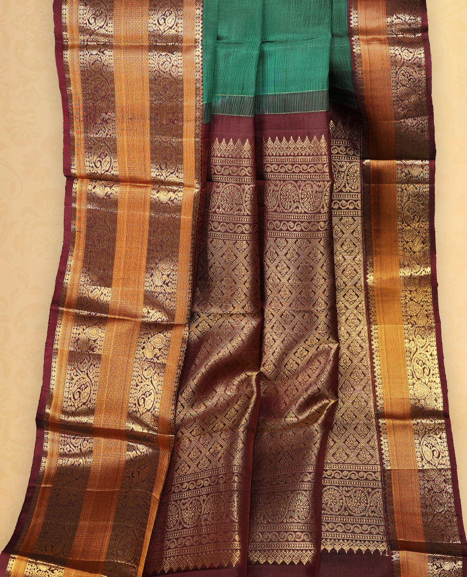 Bottle green pure Kancheepuram saree with gold zari Mayoora Chakra and diamond motifs on the body, contrast brown Kalakshetra border, grand pallu, and matching blouse.