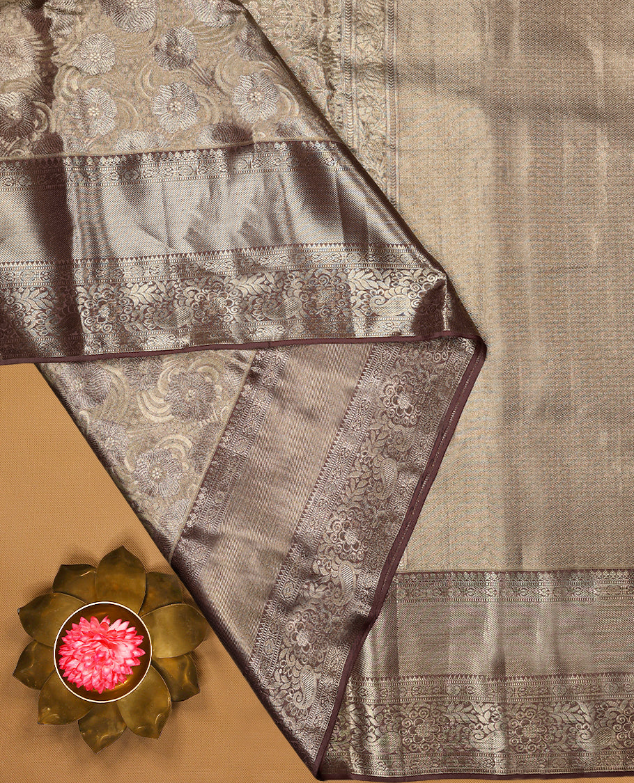 Pastel brown Colour Kancheepuram tissue silk saree adorned with intricate silver and pastel brown Zari floral motifs on the body, gracefully complemented by a traditional mango and floral design border, and paired with a matching blouse.