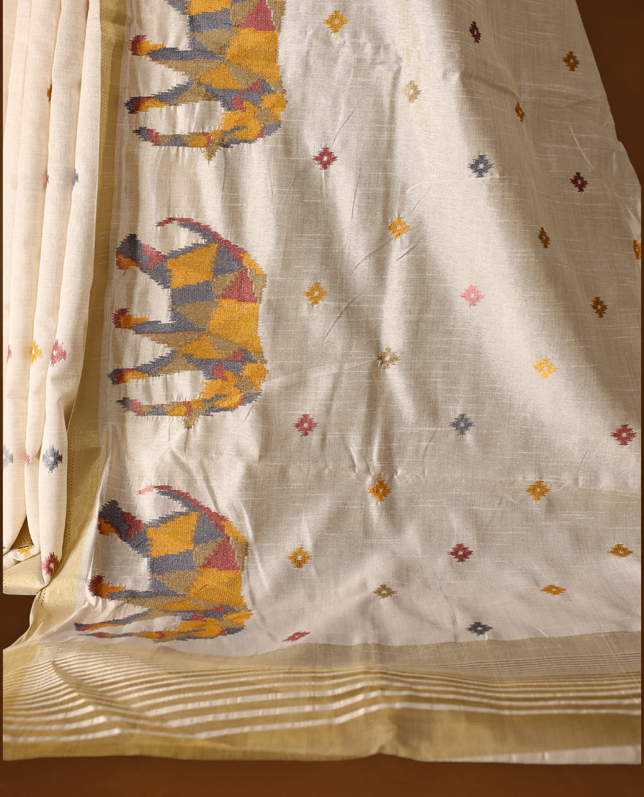 Cream colour Tussar saree adorned with multicolour geometric elephant motifs and delicate thread buttas across the body, enhanced with a subtle gold zari border, paired with a matching blouse.