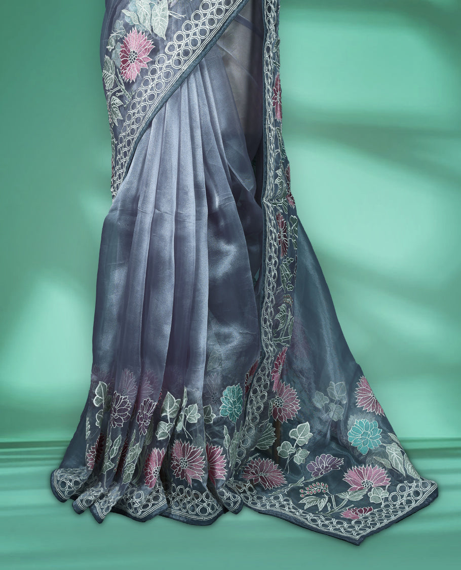 Grey colour organza designer saree featuring delicate pastel floral embroidery in pink, mint green, and white across the body, with a scalloped border accentuated by floral threadwork, and a gracefully embroidered pallu paired with matching blouse.