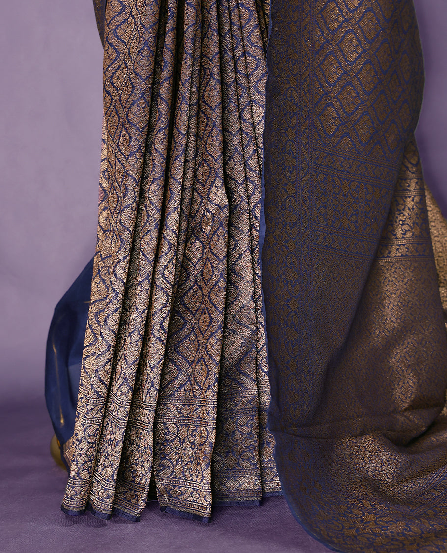 Navy Blue colour semi Banaras Katan saree featuring an antique Gold zari jacquard body, complemented by a self colour traditional border with a floral kodi design, paired with a matching blouse