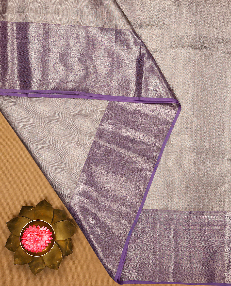 Pastel lavender Colour Kancheepuram tissue silk saree embellished with intricate silver zari work on the body, elegantly enhanced by a lavender traditional Chakkram and floral kodi design border, and paired with a matching blouse.