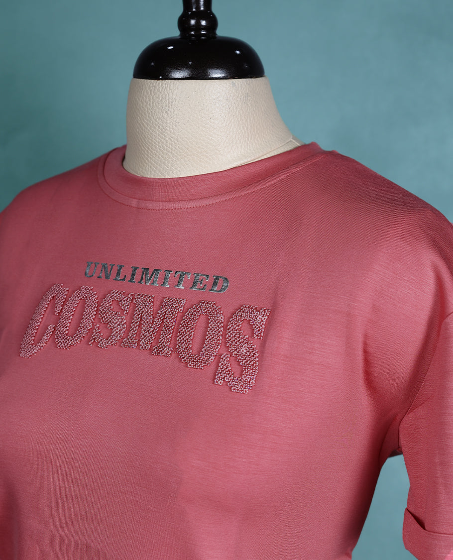 Rose pink cropped T shirt with short sleeves and rolled cuffs, featuring a subtle shimmer design on the front.