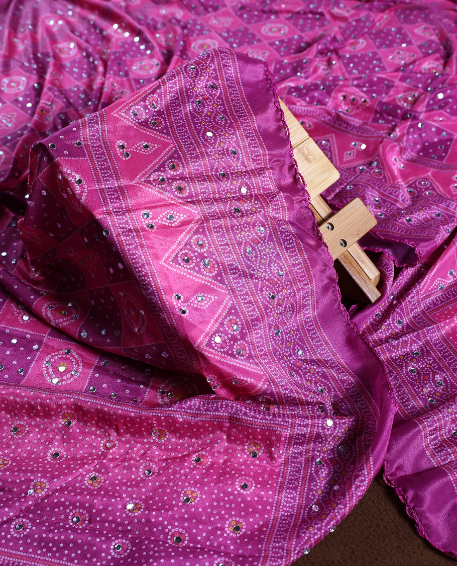 Magenta colour churidhar material adorned with intricate bandhani patterns and sparkling mirror work, paired with a plain matching bottom and elegant dupatta, perfect for festive gatherings and traditional celebrations.