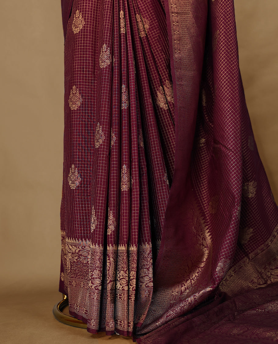 Maroon coloured semi Banaras georgette saree featuring golden Zari checks with floral motifs on the body, complemented by a self coloured traditional border with floral kodi design and a matching blouse.