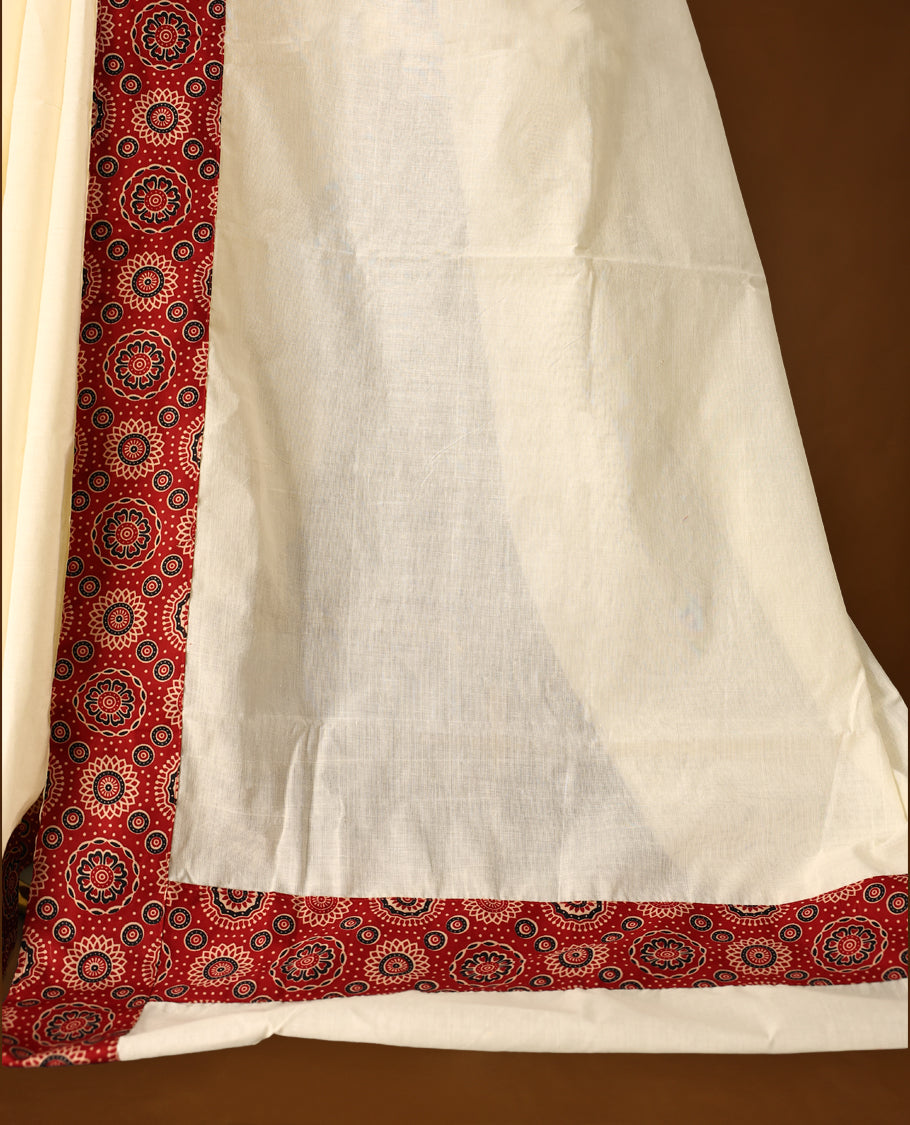 off white saree with a striking red printed border. The border features circular floral motifs in black and cream, with dotted detailing radiating outward, creating a traditional yet vibrant design