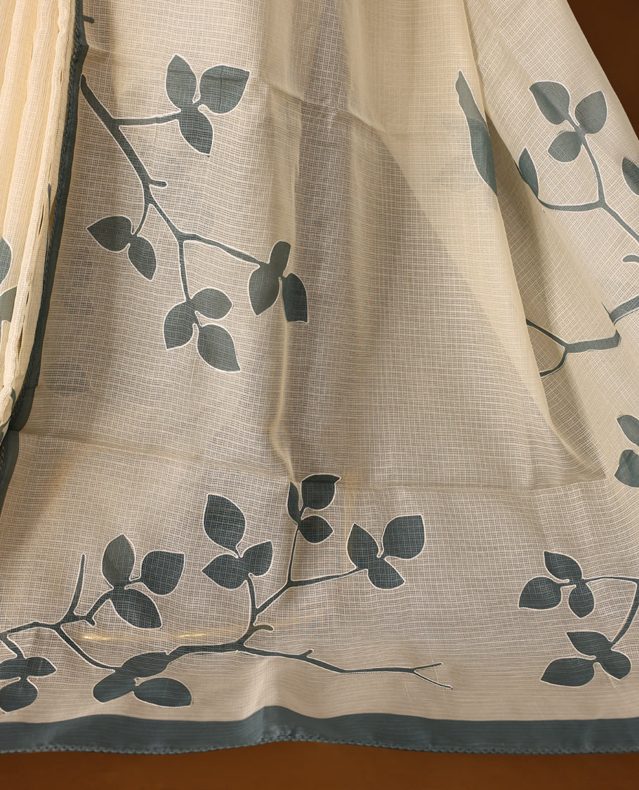 Cream colour Tussar cotton Kota saree featuring elegant stone blue leafy branch motifs across the body, accentuated with a subtle stone blue border, and paired with a matching blouse for a graceful and minimal look.