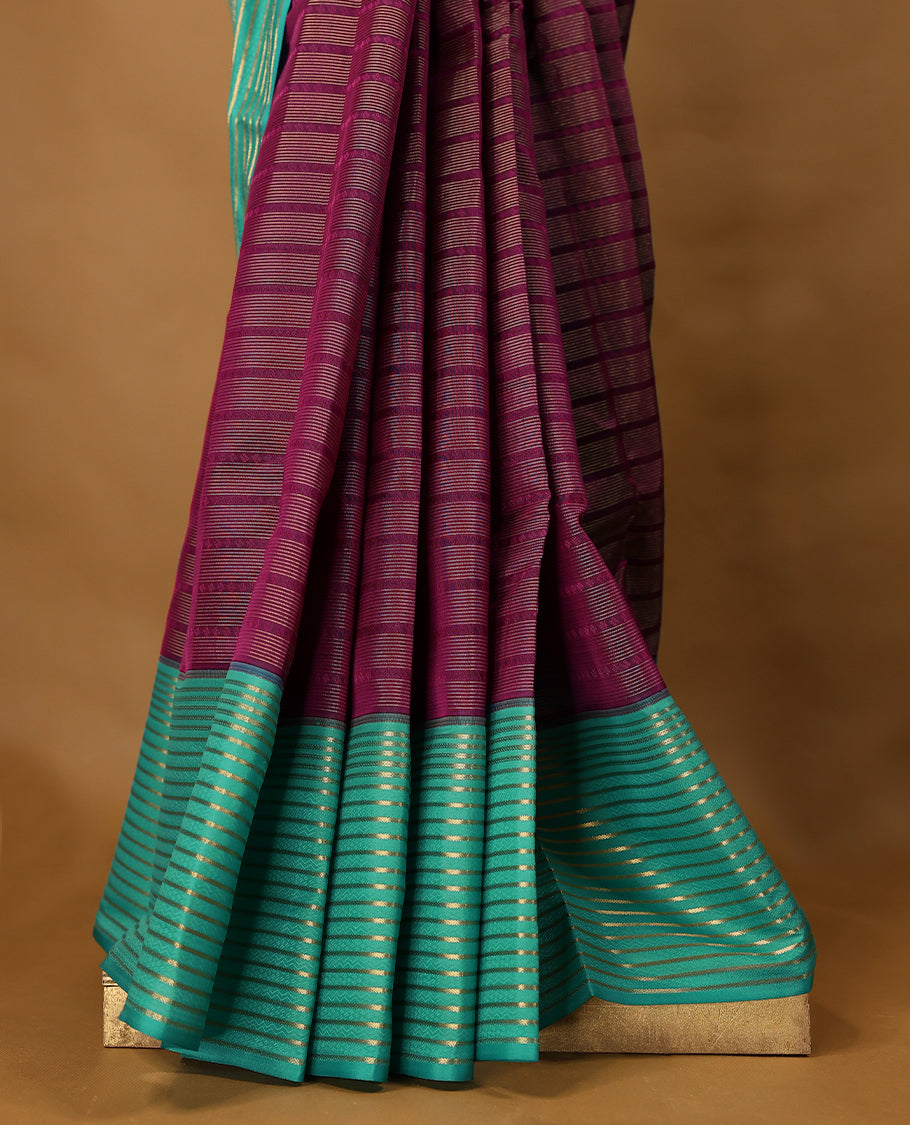 Grape coloured soft silk saree, adorned with golden zari stripes across the body, paired with a contrasting aqua-coloured border embellished with intricate golden zari work, paired with a matching contrast blouse