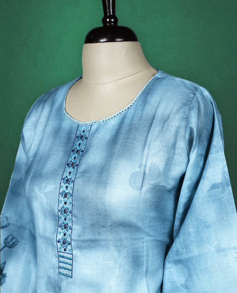 Light blue cotton kurti featuring a serene watercolour floral design near the hem and sleeves, complemented by a round neckline with vertical embroidery detail and three quarter sleeves, graceful pick for a relaxed yet refined look.