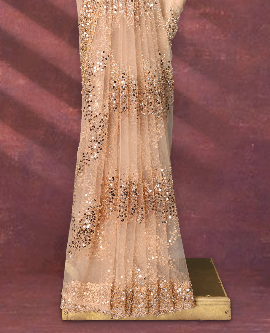Pastel peach colour net designer saree embellished with all over shimmering sequin work in diagonal patterns and a heavily sequined border, exuding glamour and elegance, paired with a matching worked blouse for a striking look