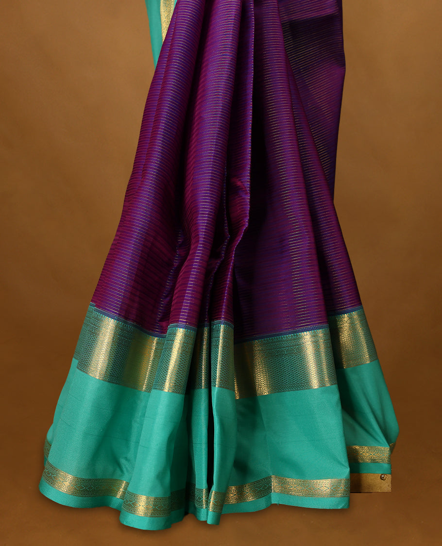 Purple Colour soft silk saree adorned with golden zari stripes on the body, complemented by an aqua colour traditional border and a matching contrast blouse