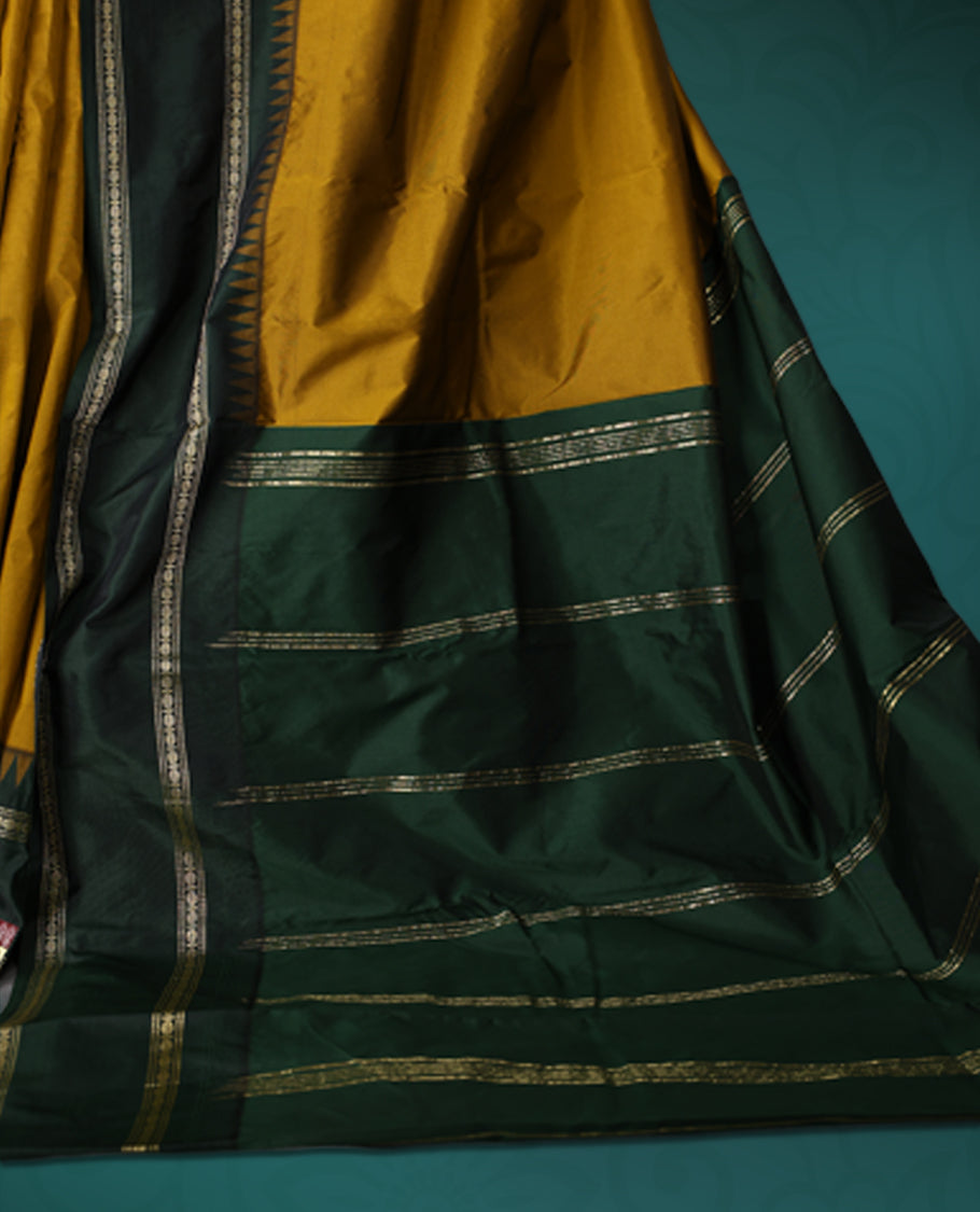 Mustard semi silk saree with plain body, vibrant deep green pallu and matching green border adorned with golden zari, accented with temple motifs along the edges, Paired with a matching blouse, perfect for festive occasions.