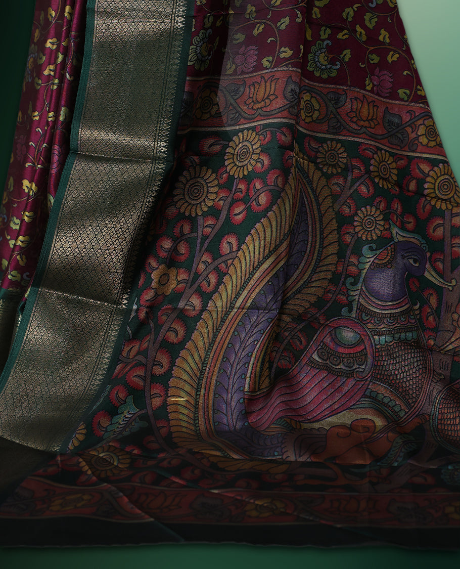 Rich Grape colour saree featuring intricate floral prints across the body, highlighted with a woven Green zari border, complemented by an artistic Kalamkari inspired pallu design, and paired with a matching blouse
