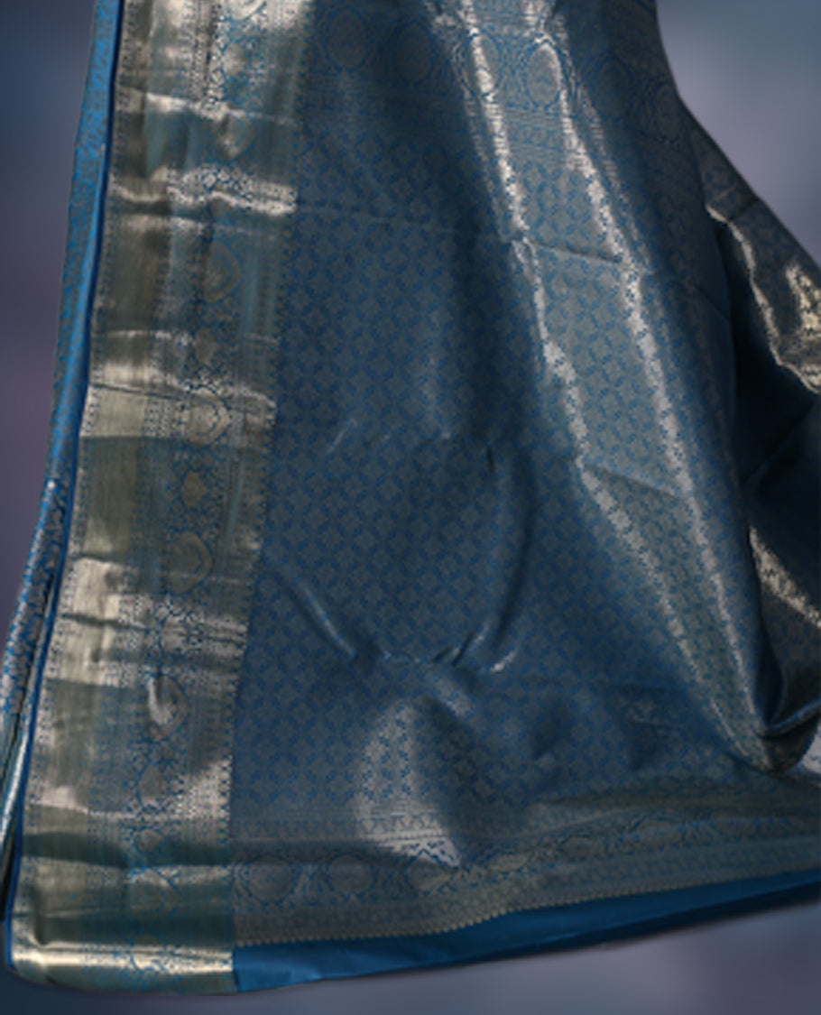 Steel blue semi silk brocade saree featuring intricate silver brocade motifs across the body, enhanced by a gleaming silver woven border and pallu, Paired with a matching blouse for a refined traditional look.