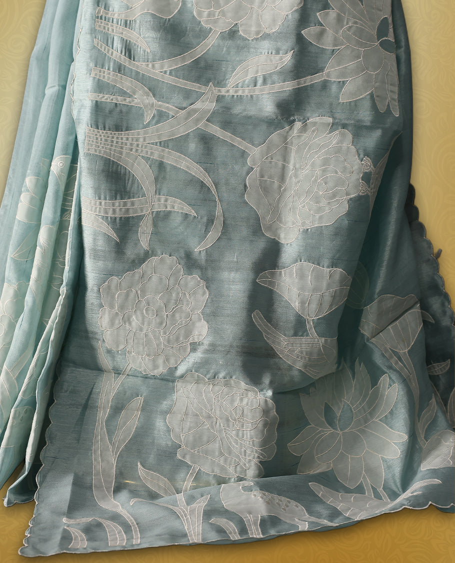 Sky Blue colour semi tussar saree adorned with elegant white applique work in leaf and floral designs across the body and border, paired with a matching blouse.