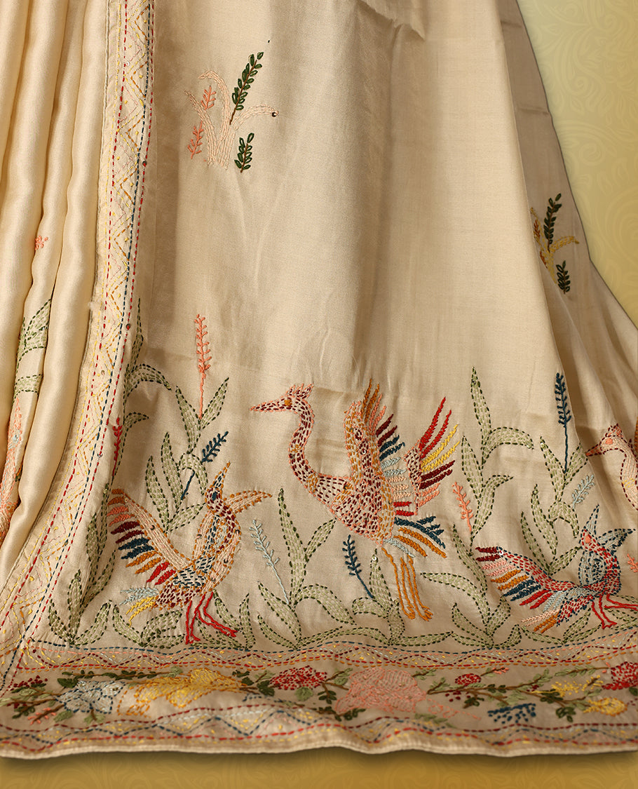 Cream colour pure tussar saree adorned with delicate Peach and green floral embroidery along the border and scattered motifs across the body, paired with a matching blouse.