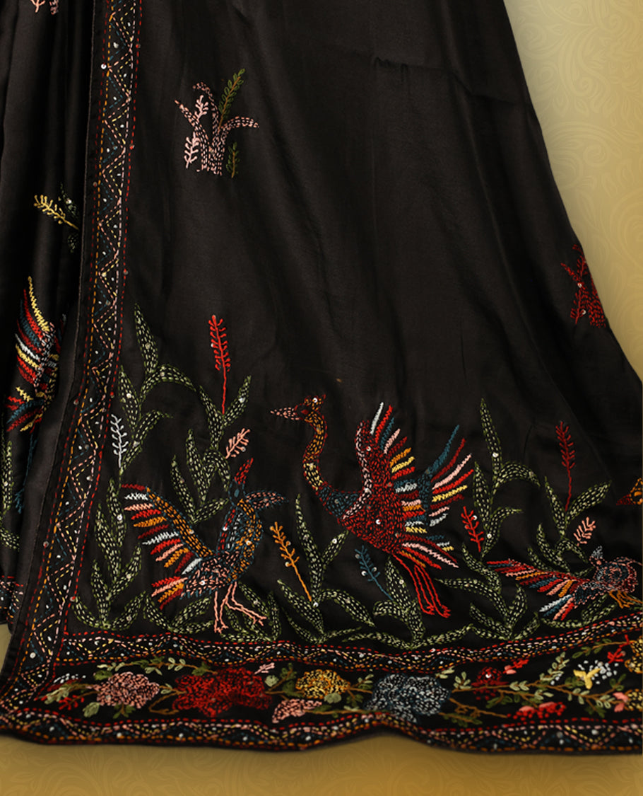 Black colour pure tussar saree adorned with delicate multicolour floral embroidery along the border and scattered motifs across the body, paired with a matching blouse.