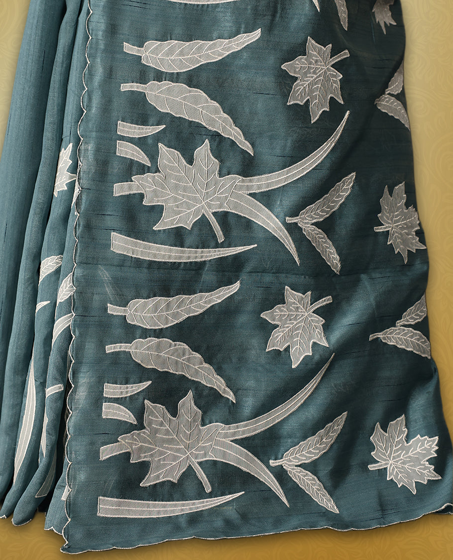 Teal colour semi tussar saree adorned with elegant white applique work in leaf and floral designs across the body and border, paired with a matching blouse.