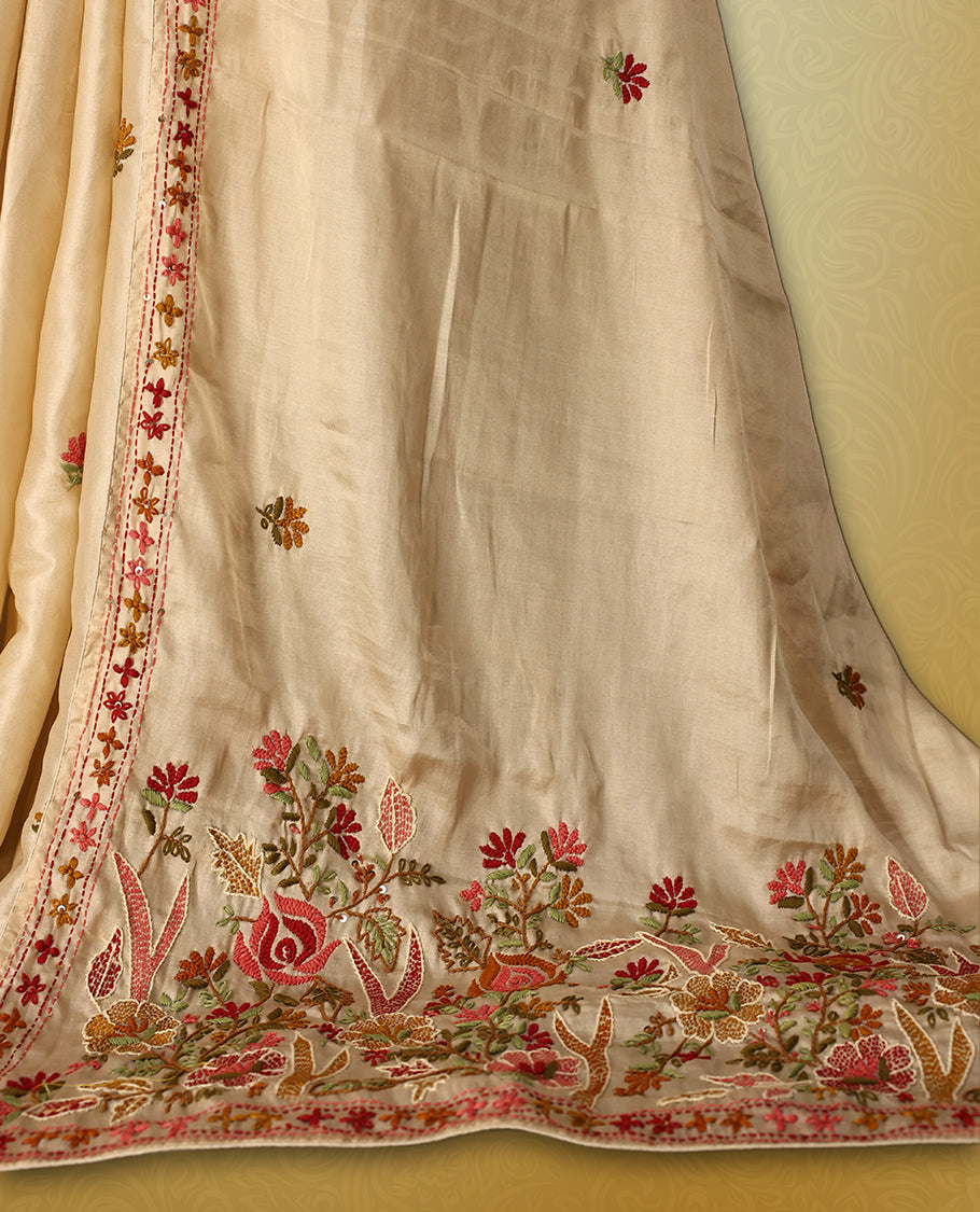 Cream colour pure tussar saree adorned with delicate pink and green floral embroidery along the border and scattered motifs across the body, paired with a matching blouse.