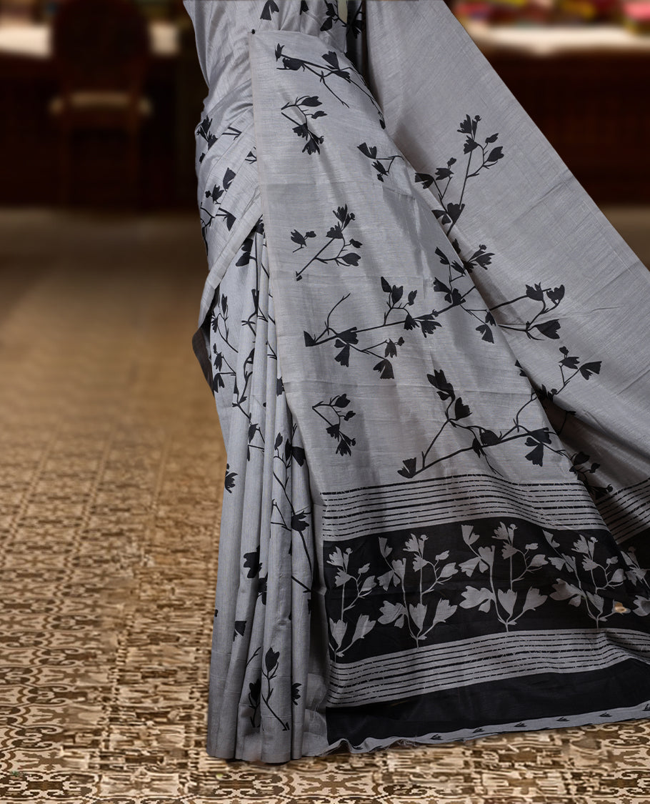 Pastel Grey colour Semi tussar silk saree adorned with black floral prints on the body and an elegant pallu & Comes with a matching blouse piece for a classy look.