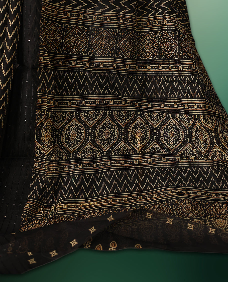 Black colour saree adorned with golden zig zag patterns across the body, complemented by a richly designed traditional pallu, and paired with a matching blouse