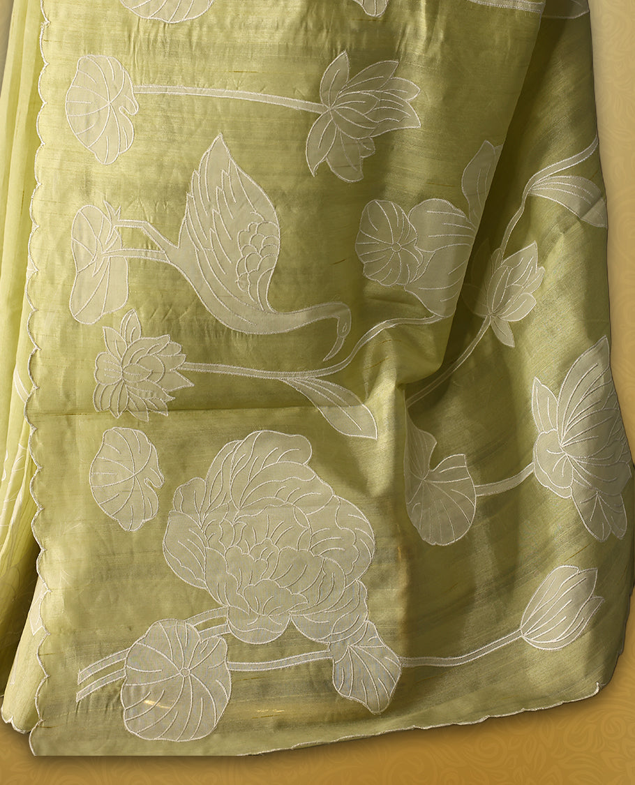 Pastel yellow colour semi tussar saree adorned with elegant white applique work in leaf and floral designs across the body and border, paired with a matching blouse.