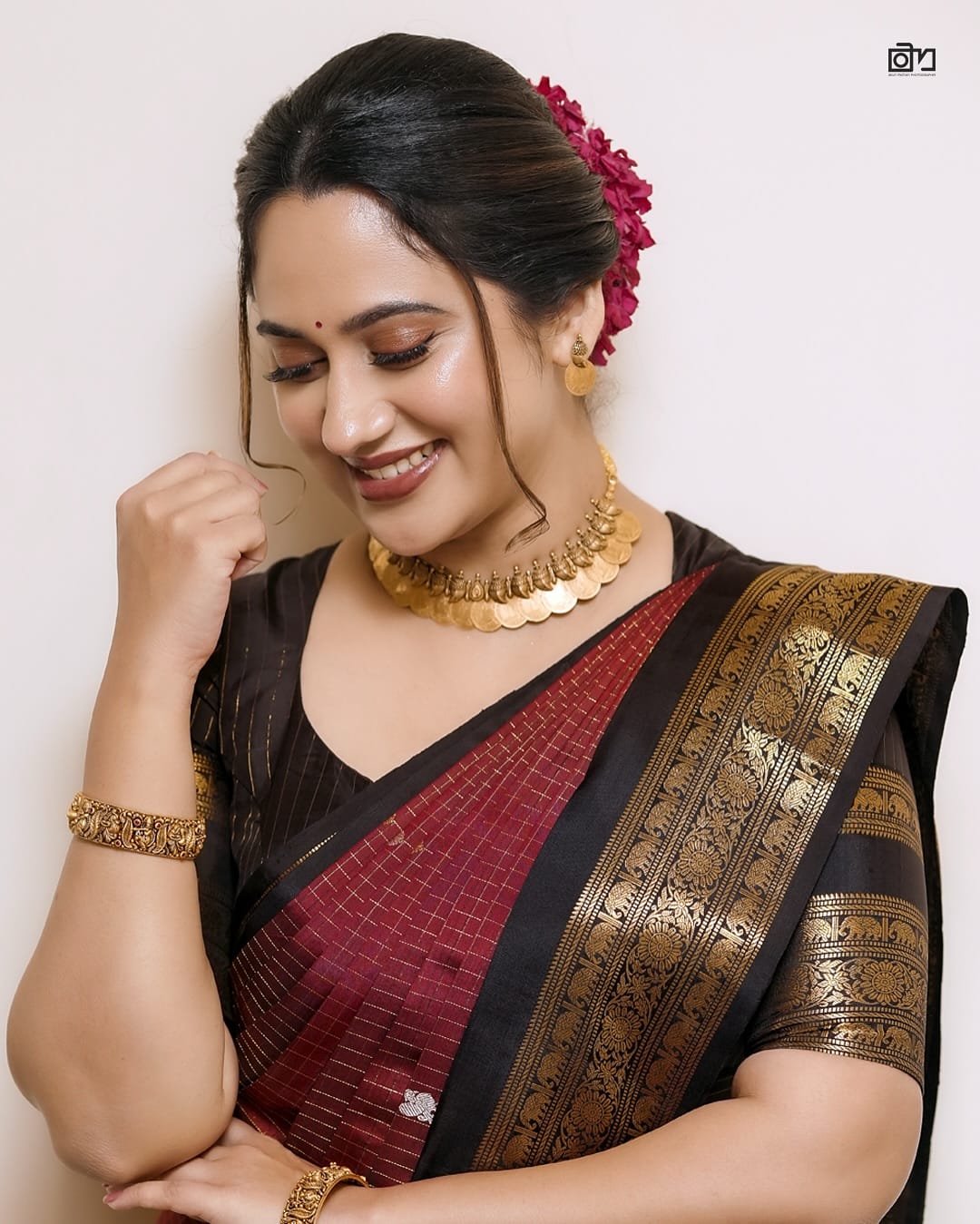 Elegant black and maroon pure Kancheepuram silk saree featuring gold zari elephant & floral brocade border rich maroon body with gold checkered patterns and Gold & Silver colour Peacock Motifs, traditional pallu paired with matching blouse