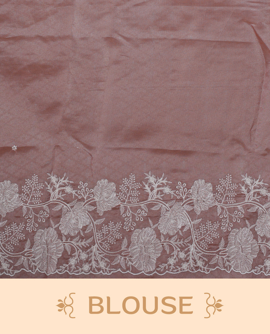 Pastel peach colour organza designer saree featuring a subtle self patterned body and an intricately scalloped floral thread embroidered border all around, complemented by a coordinating embroidered pallu and paired with a matching blouse.