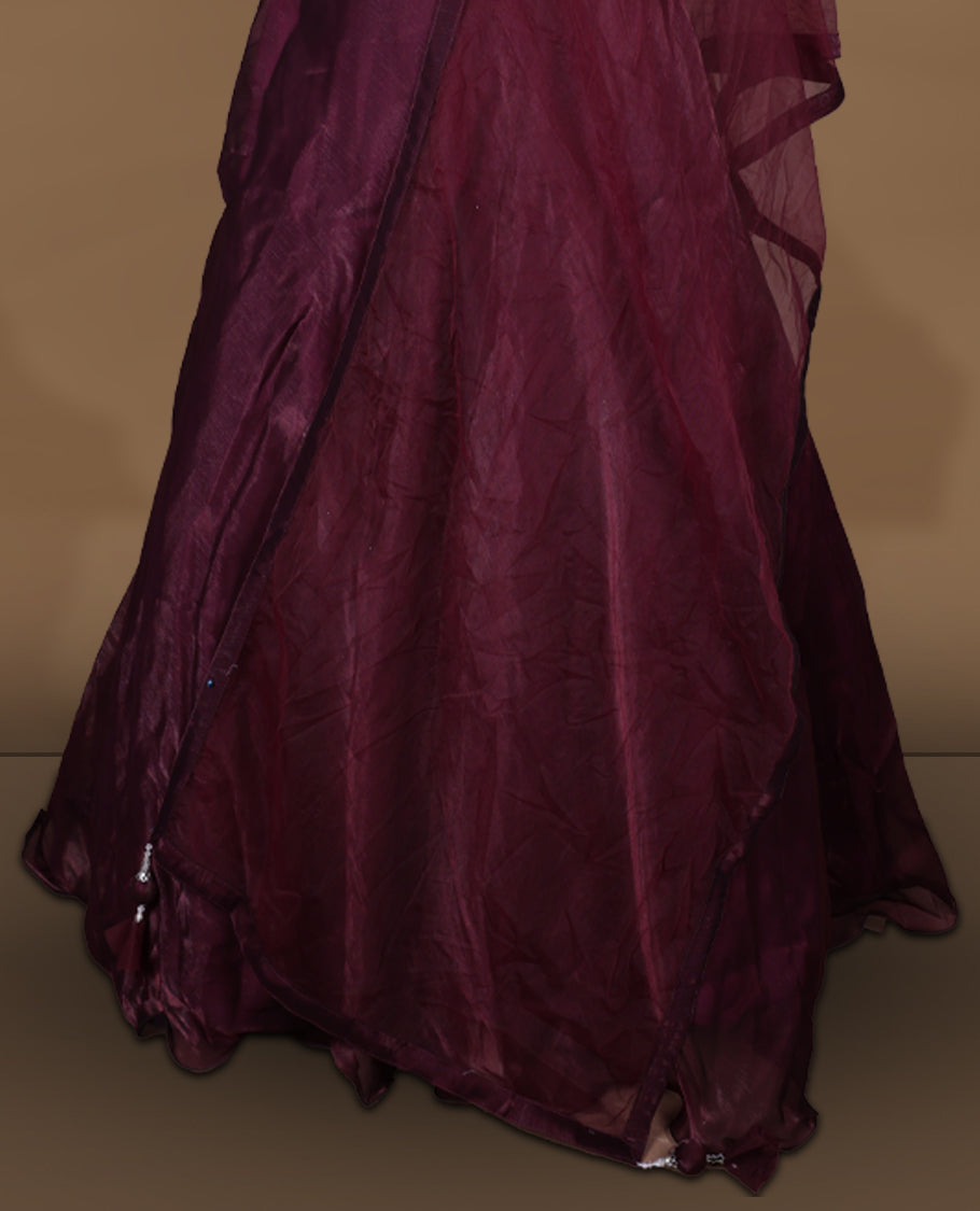 Wine colour Gown with stitched sleeveless embellished blouse featuring sheer yoke and waist detailing, matching stitched flared lehenga, and plain sheer dupatta.