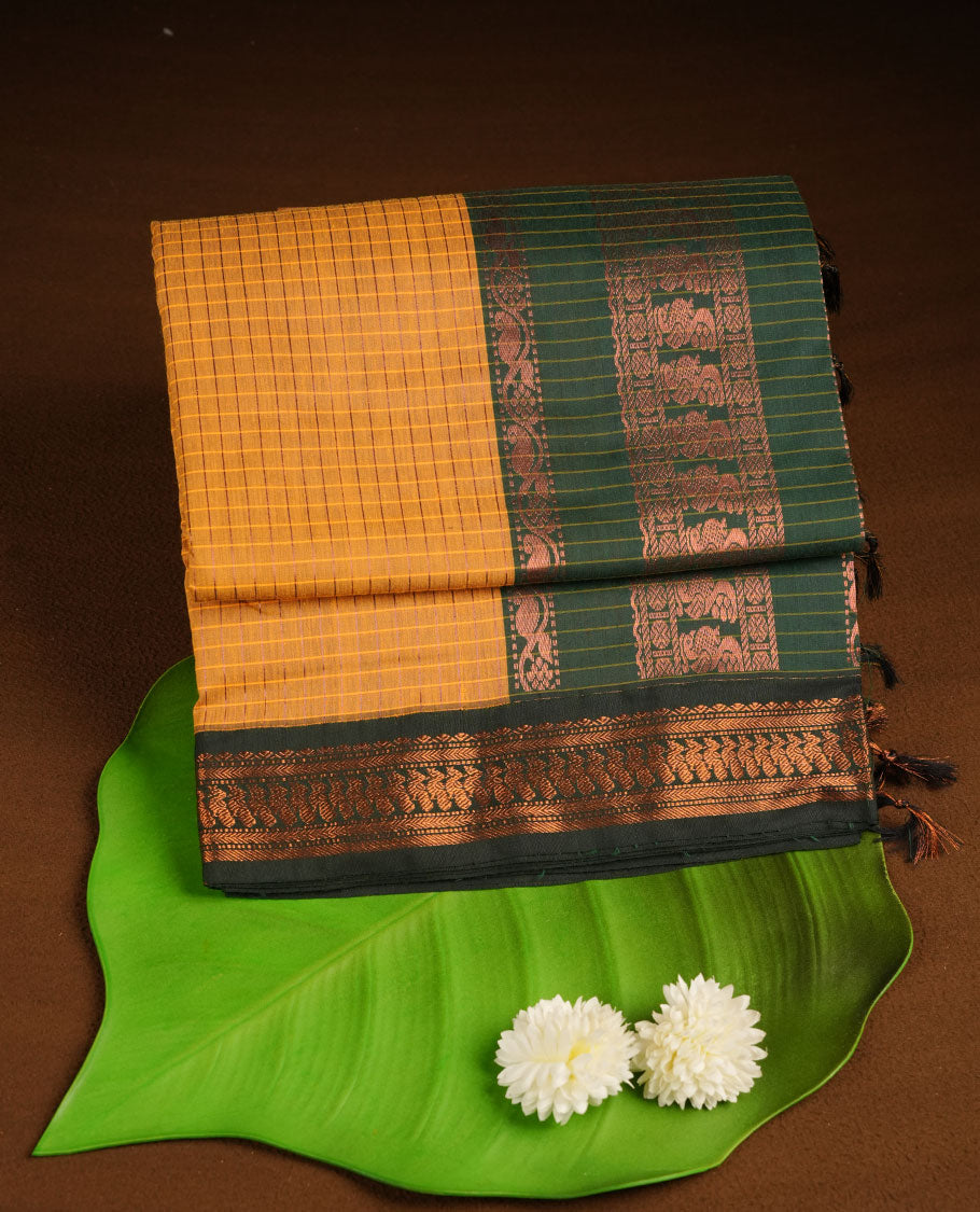 Mustard colour kalyani cotton saree featuring gold zari motifs on body, complemented by contrast green color with copper zari pattern border , paired with matching blouse piece.