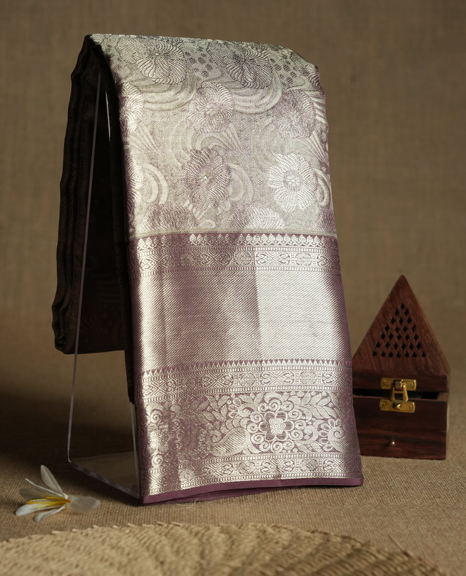 Pastel brown Colour Kancheepuram tissue silk saree adorned with intricate silver and pastel brown Zari floral motifs on the body, gracefully complemented by a traditional mango and floral design border, and paired with a matching blouse.