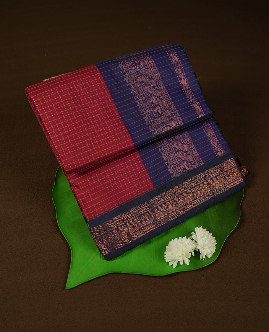 Dark Red coloured mixed Kalyani cotton saree featuring copper zari checks on the body, complemented by a Navy Blue coloured border and pallu adorned with copper zari patterns, Paired with a matching blouse.