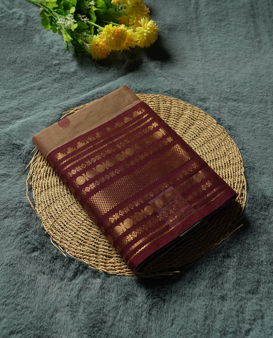 Beige Colour silk cotton saree with scattered maroon and black buttas, ornate maroon and gold zari border with geometric patterns, gold zari pallu with diamond lattice, plain beige blouse with maroon border.