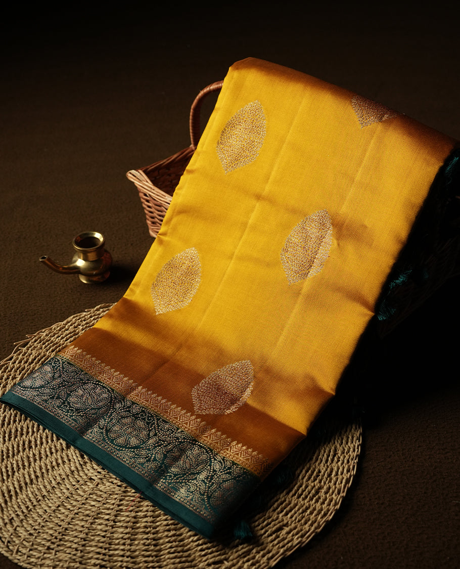 Mustard Yellow Colour Banaras Soft Silk Saree with Gold Zari Oval Buttas, Intricate Multi-Layered Floral Border, Grand Pallu with Ornate Lotus and Vine Motifs in Teal and Gold Tones, and Matching Teal Blouse.