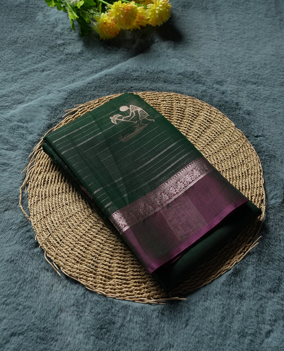 Green Colour silk cotton saree with scattered gold Warli animal motifs, gold horizontal stripes, ornate pink and gold zari border with floral patterns, gold zari pallu with diamond lattice and Warli dancer motifs, wine purple blouse.