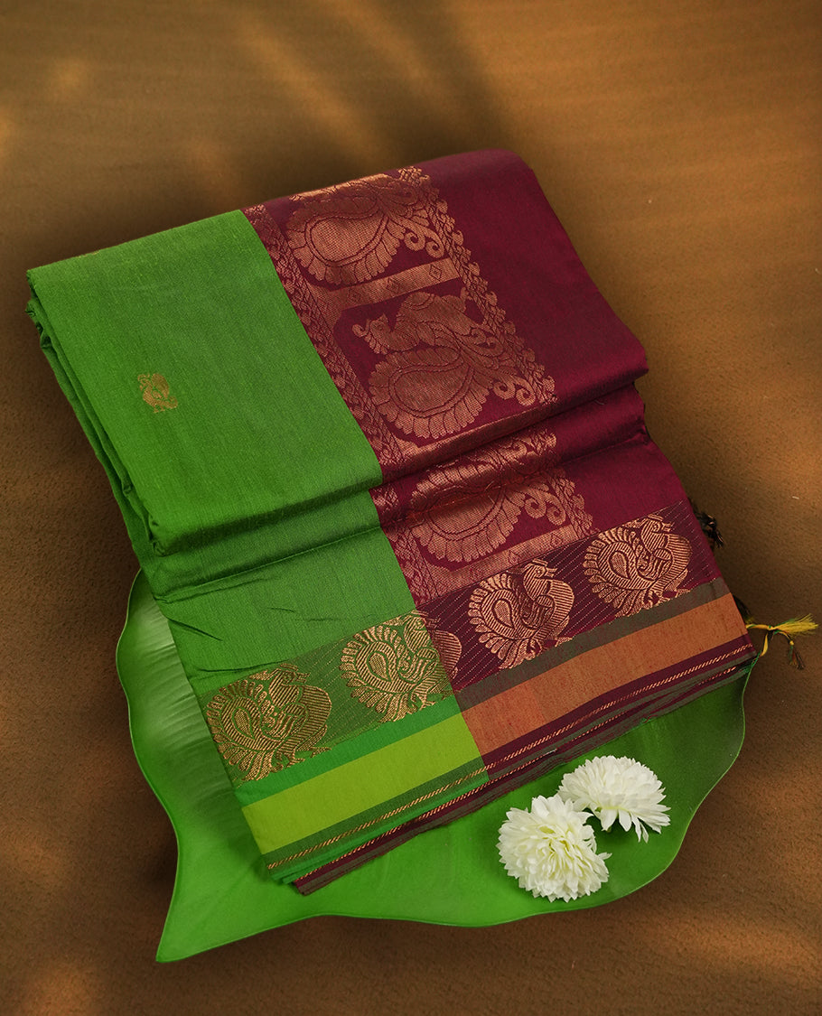 Parrot green colour Kalyani Cotton saree in deep maroon with golden peacock motifs, paired with a contrasting maroon border featuring intricate peacock zari work & Comes with a matching blouse piece.