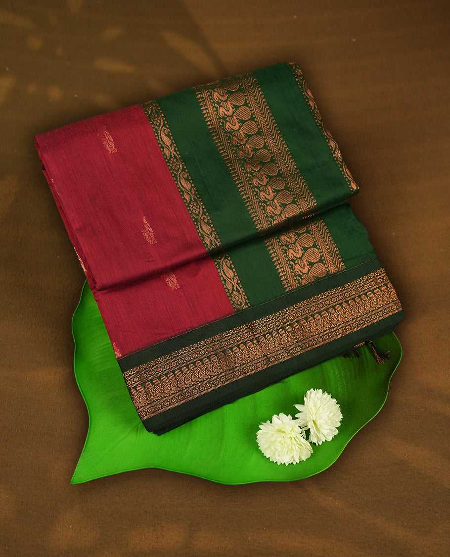 Maroon colour Kalyani cotton saree with subtle zari motifs all over, paired with a contrasting green rich copper zari woven border and pallu & comes with a matching blouse piece.