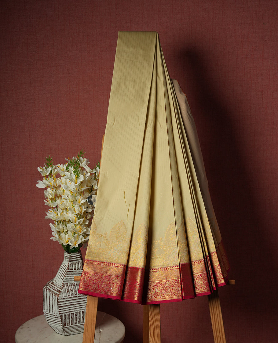 Ivory Semi Silk Saree with gold zari striped body and peacock motifs, complemented by a contrasting rani pink pallu and border in gold zari with traditional motifs, paired with a matching blouse piece