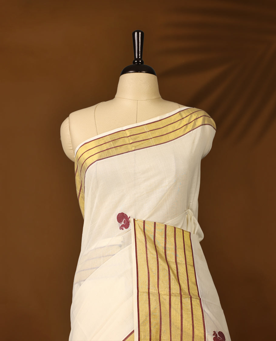 Elegant pure handloom cotton Kerala saree with a cream base, gold zari stripes, maroon & gold floral motifs. Paired with a matching blouse, it’s perfect for festive celebrations and traditional occasions.